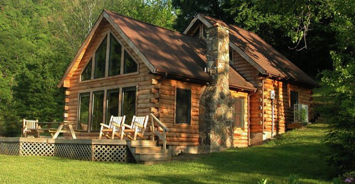 An exterior view of a large log cabin, surrounded by lush forest