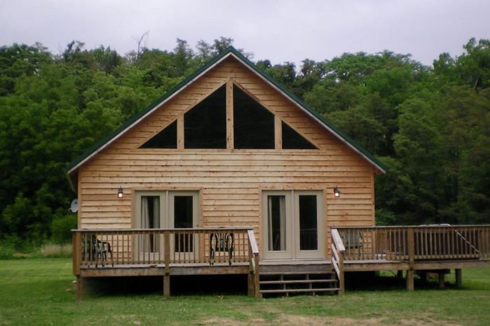 Exterior of log cabin with large windows and surrounding forest