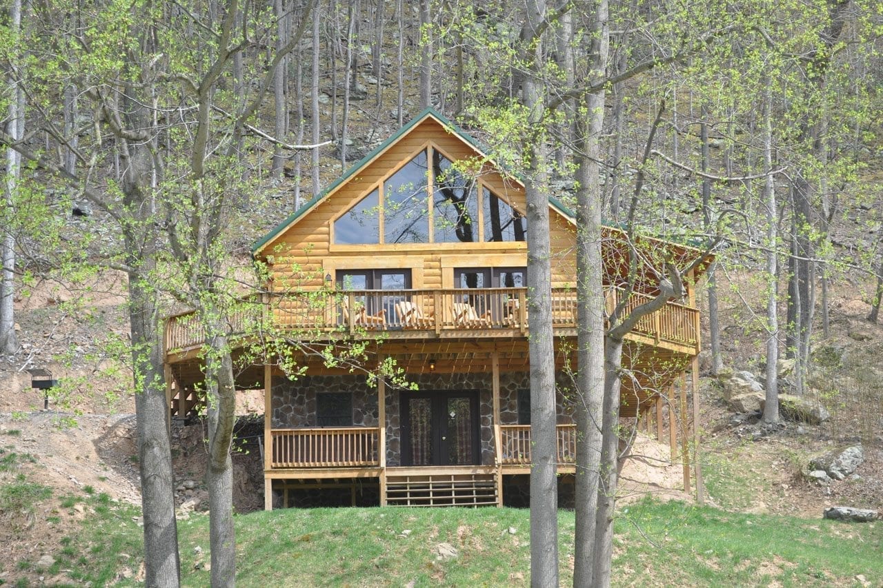 Exterior view of two story cabin with large windows and outdoor decks sitting between trees