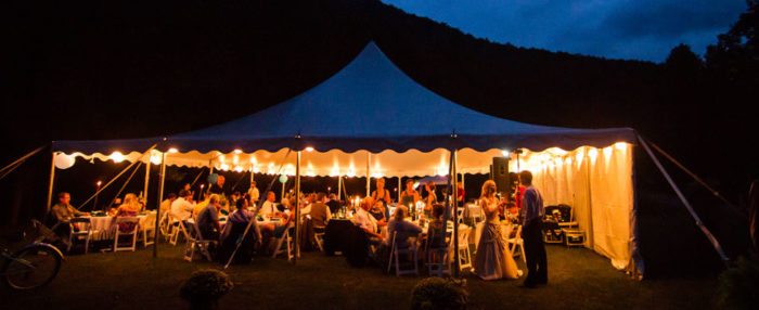 An evening reception underneath a lighted outdoor tent.