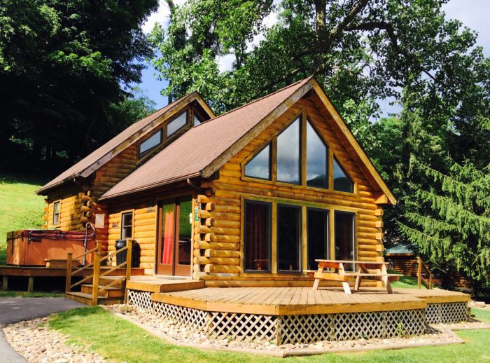 Log cabin with large windows and outdoor hot tub.